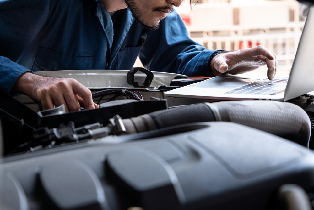 Vehicle technician running diagnostic software on laptop over modern car engine to assess used car repair costs