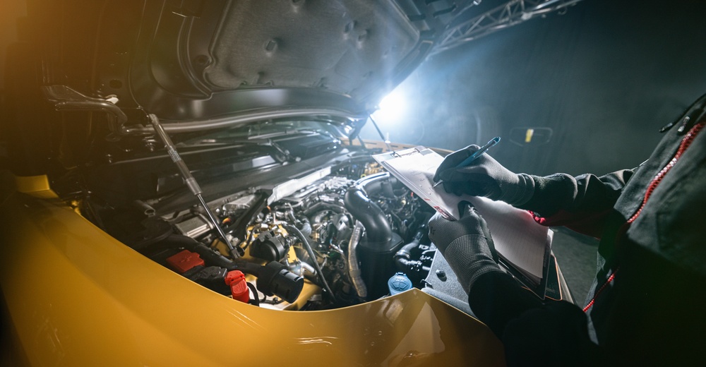 Vehicle technician inspecting engine bay with inspection clipboard for warranty claims assessment